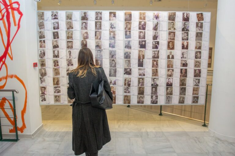 Frau steht vor einer Tafel mit 120 Porträtfotos